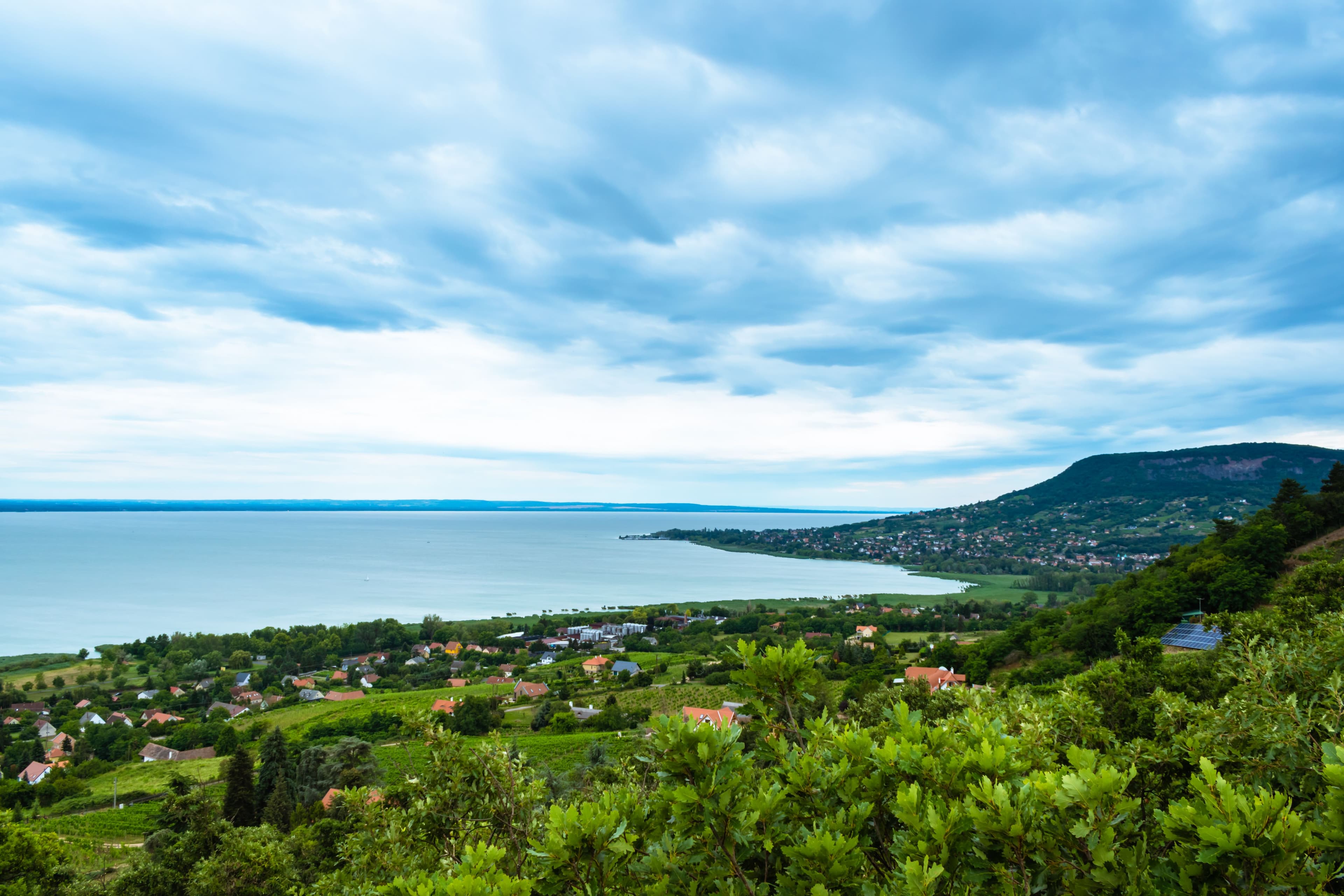 Légi kilátás egy szőlőültetvényekkel körülvett balatoni borvidéki településre, dombokkal és panorámás rálátással a tóra